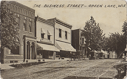 10024-The Business Street, Green Lake Wis. Looking south down Mill Street from Water Street you can see the Green Lake State Bank, W.G. Cole Dry Goods Store, Eaton's Meat Market & Groceries, Tavern, Deacon Mills Hotel.-Postmarked 1910