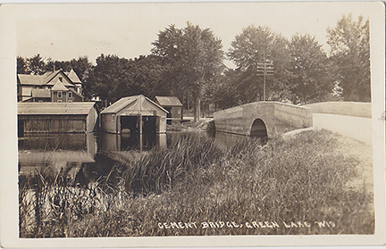 10450-Cement Bridge on South Lawson Drive. One of the first projects advanced by the residents of Dartford was the building of a bridge and causeway from the village West towards Princeton. This bridge crossing the Green Lake outlet to the Puchyan River would later become part of South Lawson Drive. Captain Pierce's Boat houses & livery office can be seen across the channel.