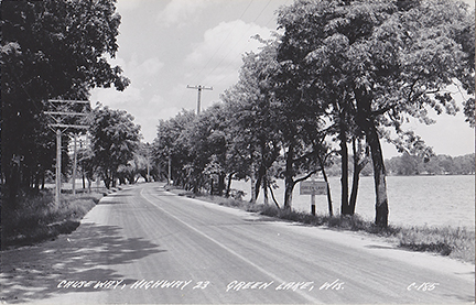 10471-Causeway, Old Highway 23-Now South Lawson Drive. This view is looking north along the original Hwy 23 (Lawson Drive) towards the causeway and concrete bridge. Population of Green Lake shows 560. The Maplewood driveway is on the left.