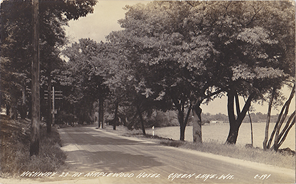 10737-Hwy 23 at Maplewood Hotel, Green Lake, Wis. This view is looking north along the original Hwy 23 (Lawson Drive) towards the causeway and concrete bridge. If you look really hard you can just see Norton's boathouses.